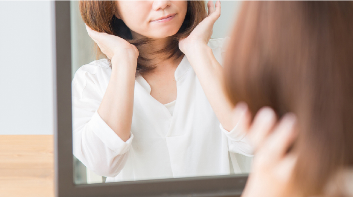 鏡の前で仕上がった髪を確認する女性。ボブスタイルの自然なツヤと軽やかな質感をチェックする様子。