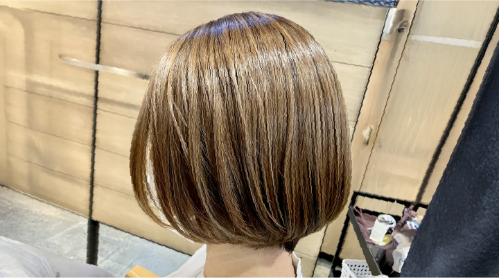 美容室で仕上がったツヤのあるボブスタイルの後ろ姿。光沢のあるカラーとまとまりのあるカットラインが特徴。