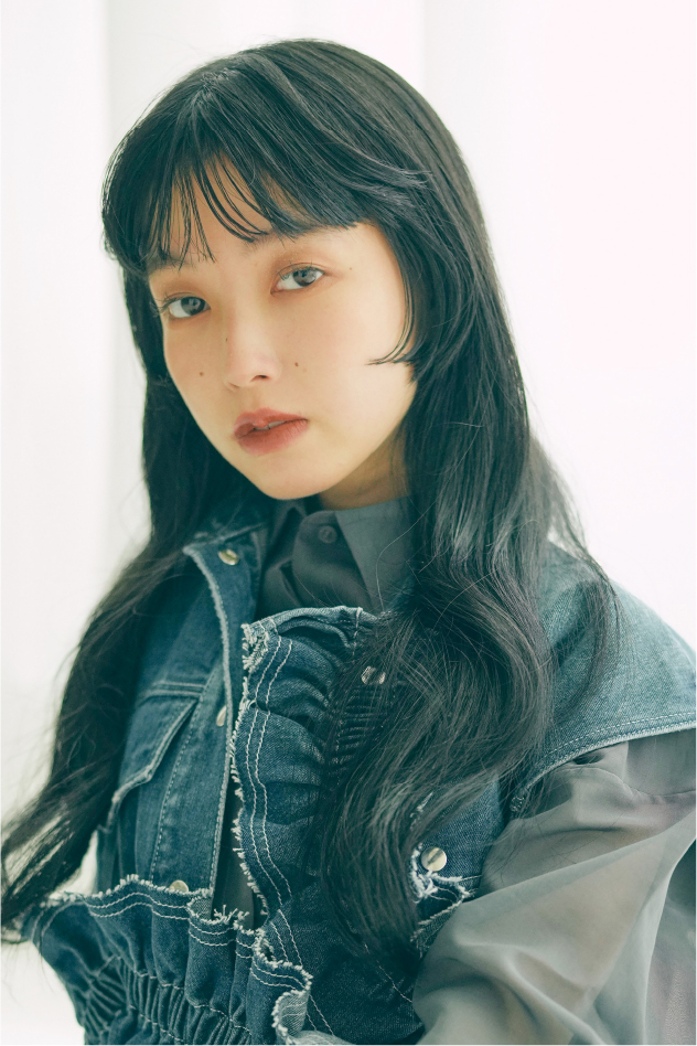 黒髪ロングヘアの女性がデニムベストを着て見つめるポートレート、ナチュラルでクールな雰囲気のスタイル写真