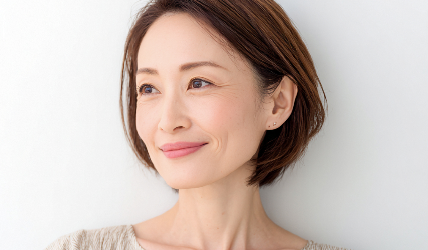 白い背景の前で、ショートヘアの女性が柔らかく微笑み、少し横を向いている明るい印象のポートレート。